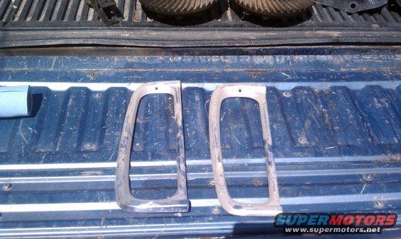 Two weathered chrome tail light bezels on a blue truck bed