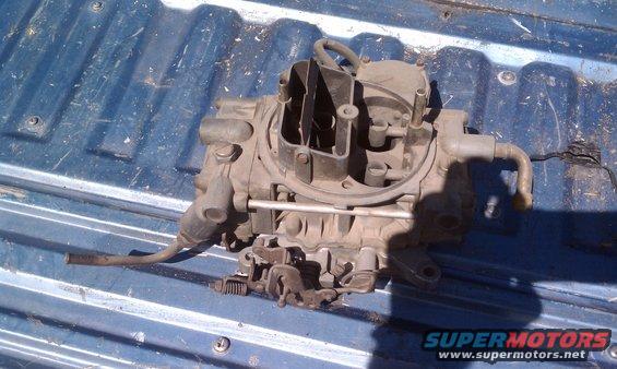 Holley carburetor with linkage and fuel lines, resting on a blue truck bed
