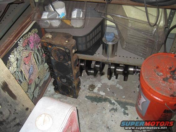 engine block and crankshaft on shelf with storage bins and an orange bucket