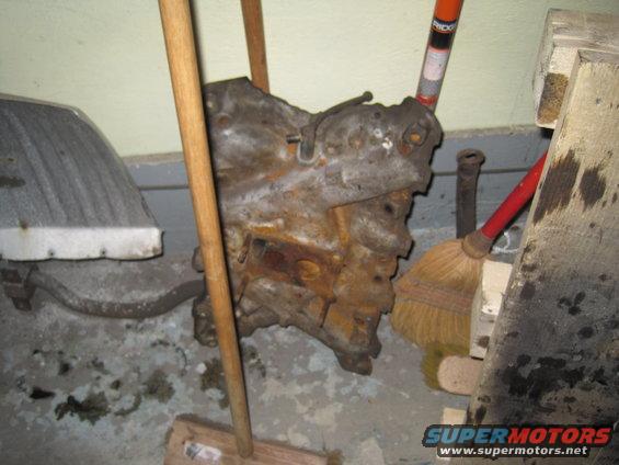 Rusted engine block with wooden handles and brooms around it