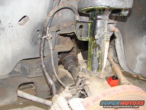 Close-up of a car's front suspension assembly, showing a strut, brake rotor, and drive axle boot