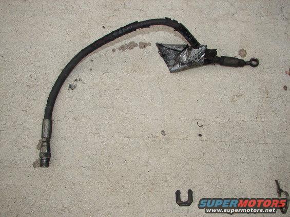 worn brake hose with metal fittings and tape on it, lying on concrete