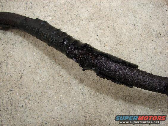 Damaged black wire harness with exposed wires and frayed insulation, resting on a concrete surface