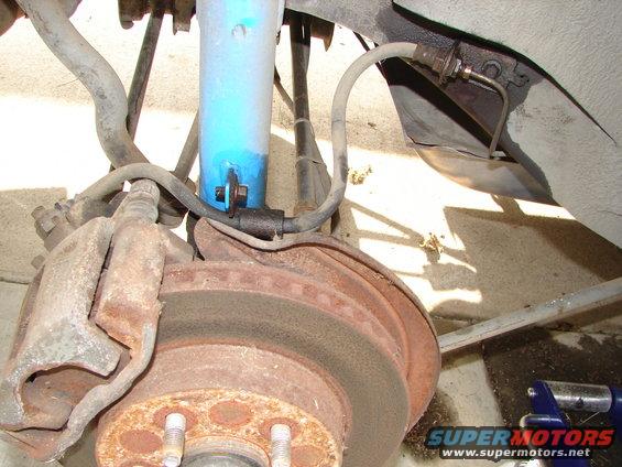 Close-up of a rusty car brake rotor, caliper, and blue shock absorber