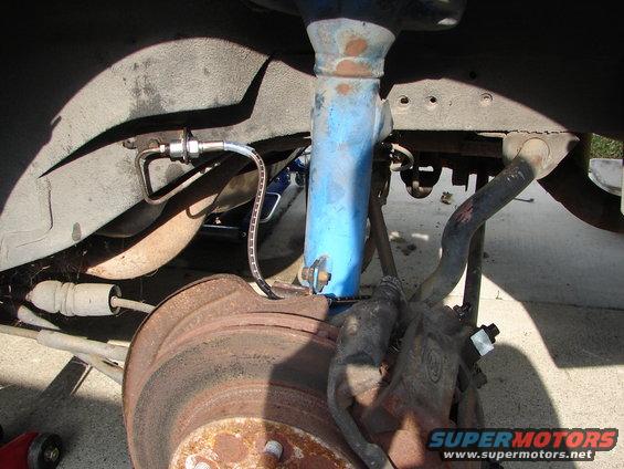 Car brake assembly with rusty rotor and blue shock absorber. Brake line visible