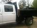 1997 Ford F-350 - A white crew cab truck with a flatbed is parked next to a dark-colored dump truck.
