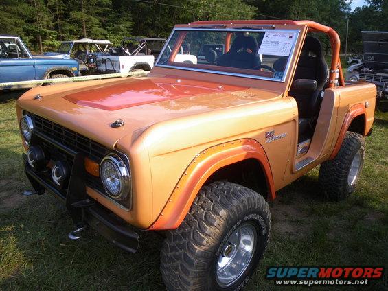 Orange Ford Bronco with roll cage and racing seats. Other Broncos are parked nearby