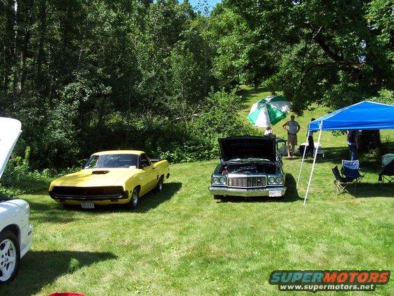 Yellow car and dark car with hoods open at an outdoor car show