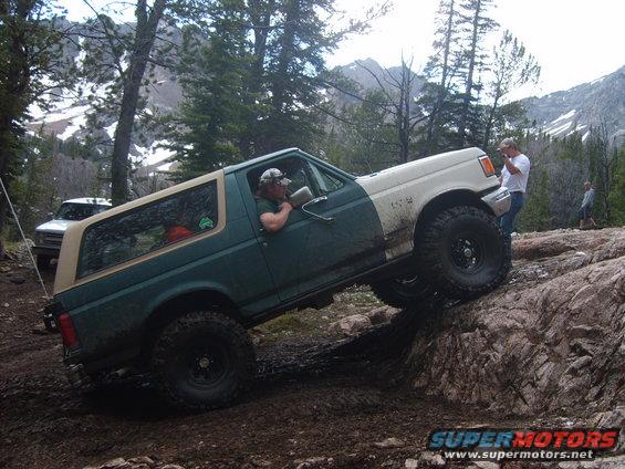 Green and tan Ford Bronco off-roading on rocks, driver visible