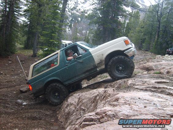 Green and white 1989 Ford Bronco climbing rocks on a trail