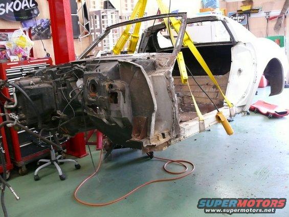 car body lifted by yellow straps, undergoing repairs in a garage