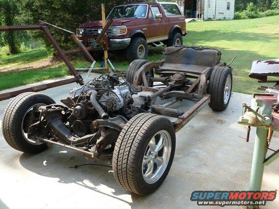 car frame with engine and wheels, maroon SUV in background