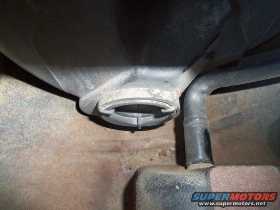 Close-up of a vehicle's fuel tank filler neck and hose. Shows some rust on the undercarriage