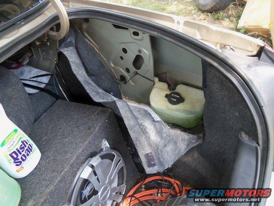 Car trunk interior with a subwoofer, bottle of dish soap, and a windshield washer fluid reservoir