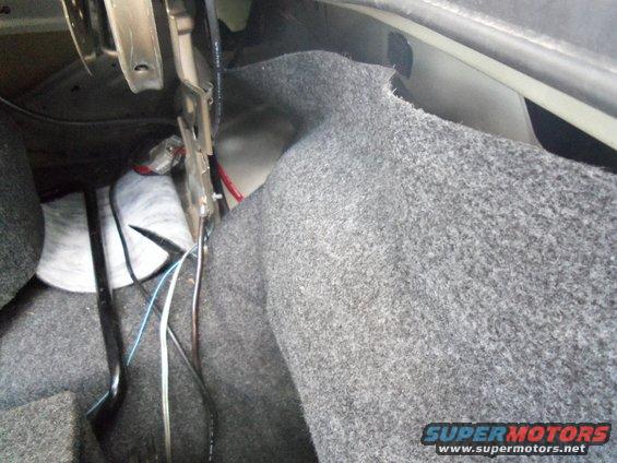 Car trunk interior with gray carpet lining, exposed wiring, and metal brackets
