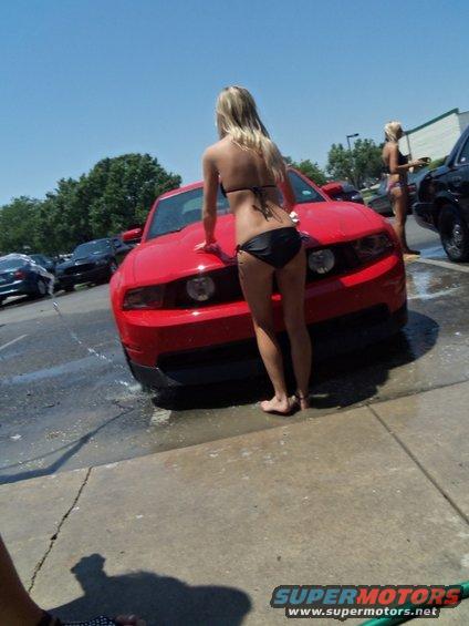 Red Ford Mustang with woman washing hood. Water on ground