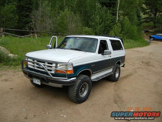 White and teal 1996 Ford Bronco with aftermarket bumper, driver's door open