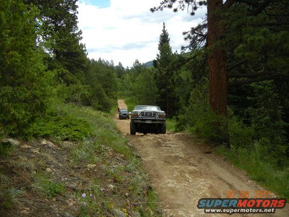 White Ford F-Series truck driving on a dirt road, rear view. Another vehicle is ahead