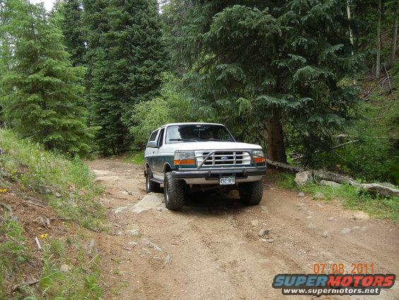 1996 Ford Bronco on a rocky dirt road surrounded by pine trees