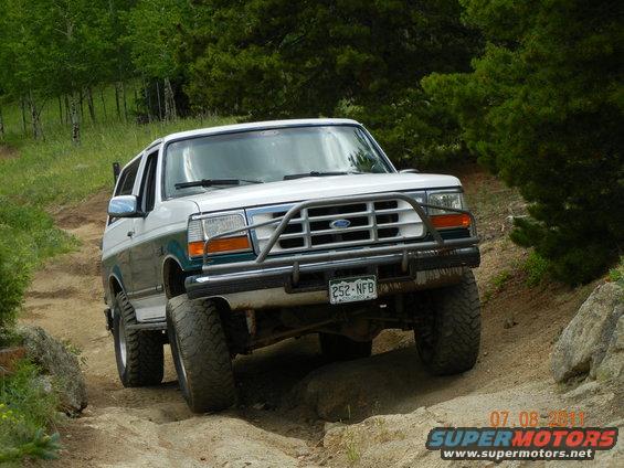 White and green Ford Bronco on a dirt trail, front view, with a brush guard