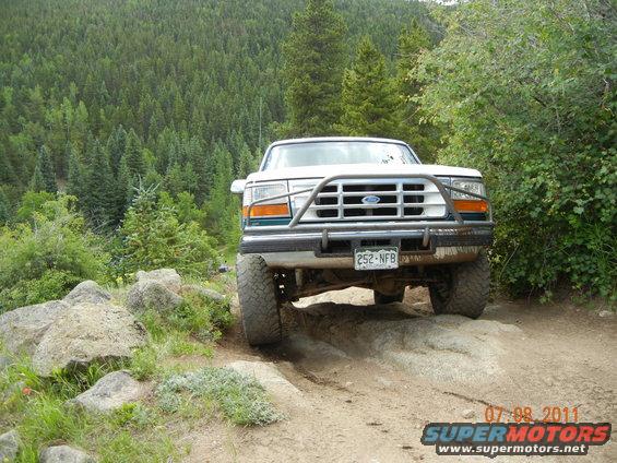 1996 Ford Bronco navigating a boulder on a dirt trail, forest in background
