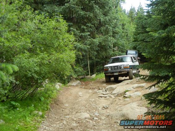 White and green 1996 Ford Bronco on a rocky trail with another vehicle behind