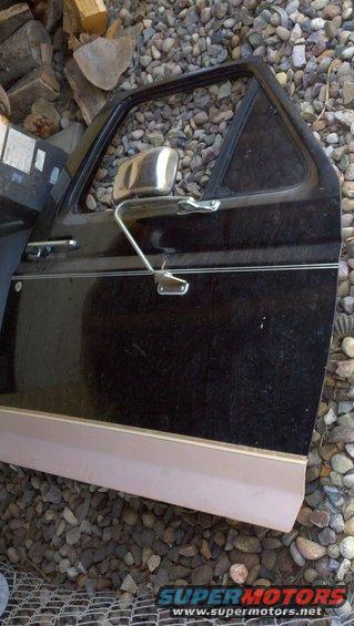 Black Ford Bronco door with chrome mirror and trim, resting on gravel