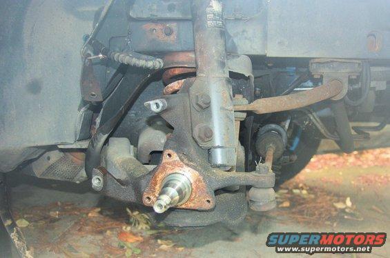 Close-up of a rusty car suspension assembly, showing the spindle and shock absorber mount