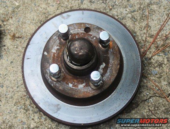 Rusty car brake rotor with four lug nuts on a concrete surface