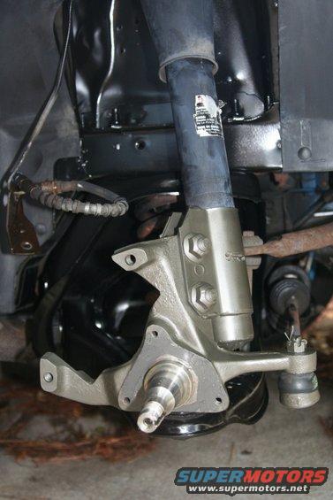 Close-up of a car's front suspension assembly, showing the spindle, brake caliper bracket, and shock absorber mount
