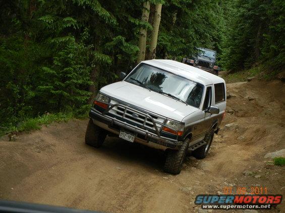 White 1996 Ford Bronco on a dirt road with a Jeep behind it