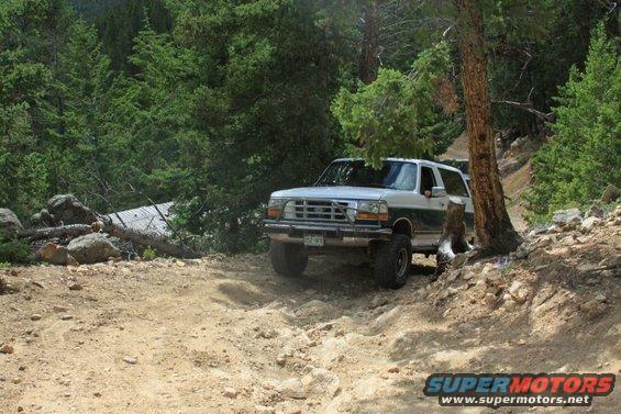 1996 Ford Bronco driving on a rocky, wooded trail