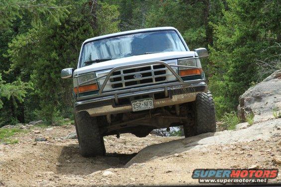 White Ford Bronco on a dirt trail, front view, with a brush guard and off-road tires