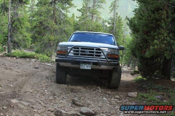 White Ford Bronco with a brush guard driving on a rocky dirt road