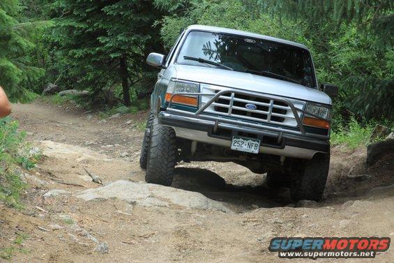 1996 Ford Bronco navigating a rough, rocky trail with trees in the background. License plate reads 252-NFB