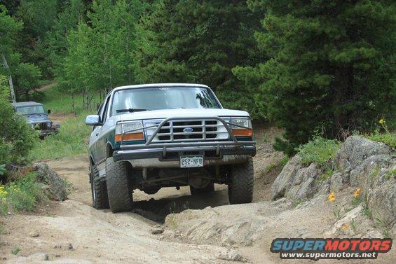 1996 Ford Bronco driving on a rocky, off-road trail with a Jeep in the background