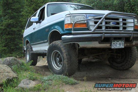 Ford Bronco with a brush guard on a dirt trail, trees in background