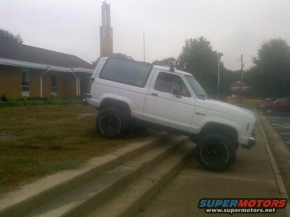 White 1988 Ford Bronco II driving up concrete stairs next to a building