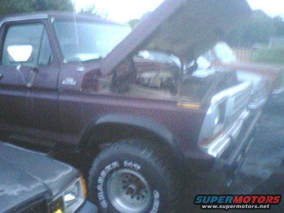Maroon Ford truck with hood open, showing engine. Another vehicle is partially visible to the left