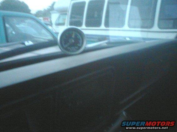 Black car hood with a gauge and racing stripes, next to a teal vehicle and a white RV