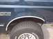 1990 Ford Bronco - Close-up of the side of a dark blue SUV, showing the fender, wheel well, and tire. The "BRONCO" badge is visible.