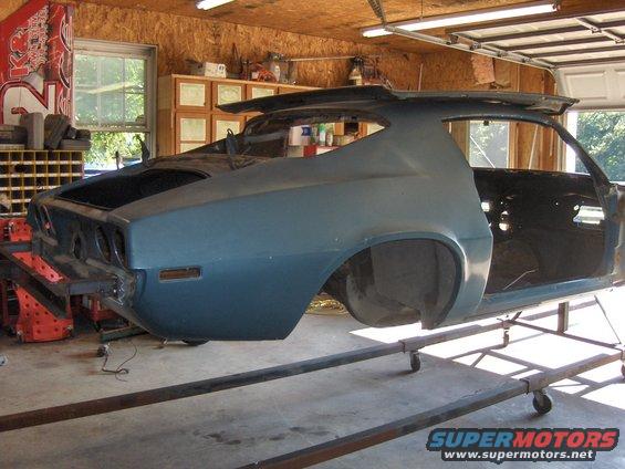 Blue 1970s muscle car body, rear view, on a stand in a garage