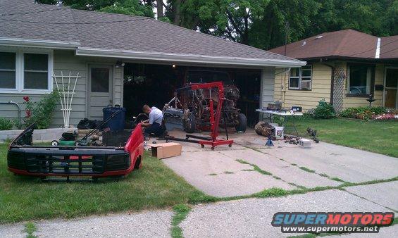 Truck front end sitting on grass, engine being worked on in garage with an engine hoist