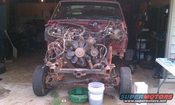 Truck chassis with engine exposed, front wheels on, in a garage