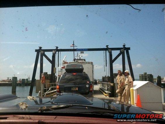 Black Jeep Cherokee with a roof cargo box on a ferry, seen from behind
