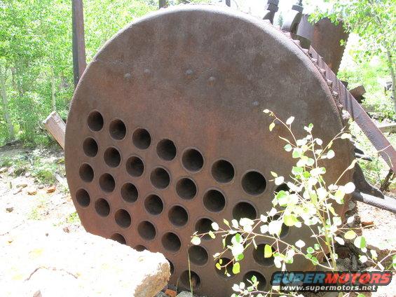 Rusty boiler part with circular holes, overgrown with plants