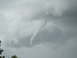 1994 Ford Bronco - Tornado funnel cloud forming in stormy grey clouds, with trees visible at the bottom left.