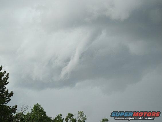 storm clouds forming a funnel shape over trees