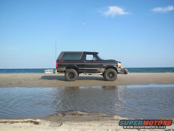 Black Ford Bronco parked on a sandy beach with the ocean in the background