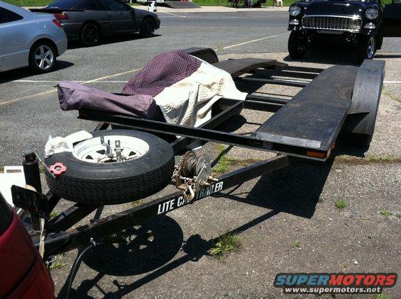 black 1955 Chevrolet Bel Air on a trailer, with a silver car and a dark coupe in the background